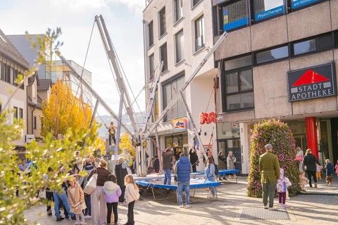 People enjoy activities on bungee trampolines in front of municipal shops and a pharmacy,