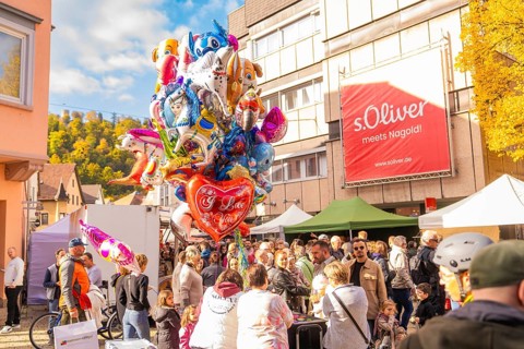 Colourful balloons over a crowd of people on a sunny market square surrounded by buildings,