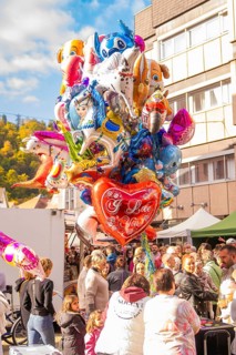 Various colorful balloons, including a heart with 'I Love You, 'float above a celebratory crowd,