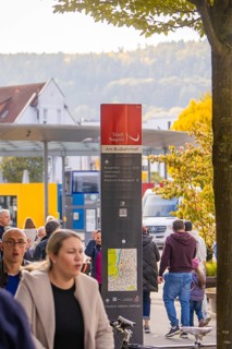 People walk past a bus stop, a signpost shows the way, Urschelherbst Street Festival, Nagold,