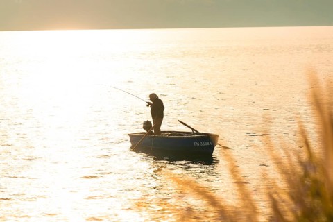 An angler fishing from a boat in the golden light of sunset, Überlingen, Lake Constance, Germany