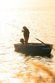 Single fisherman in a small boat fishing in the setting sun, Überlingen, Lake Constance, Germany