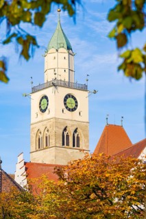 A church tower with clocks rises into the blue autumn sky, surrounded by autumn leaves, Überlingen,