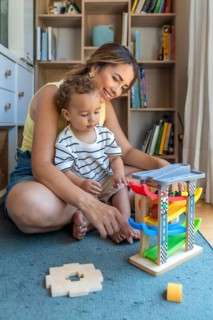 Smiling mother and son playing with a toy car and garage, enjoying quality time together in their