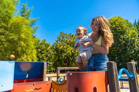 Happy mother holding her smiling son on a colorful playground game structure on a sunny summer day