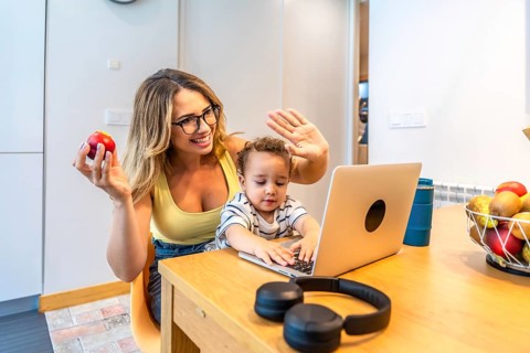 Mother and son waving joyfully at the computer during a video call while enjoying breakfast