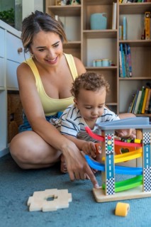Mother and baby son sitting on the floor, joyfully playing together with a colorful toy car and