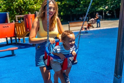 Happy mother enjoying quality time with her toddler son, playfully pushing him on a swing at the