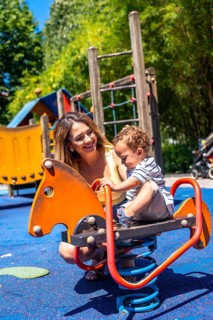Smiling mother spending time with her baby son, enjoying a sunny day at the playground, promoting