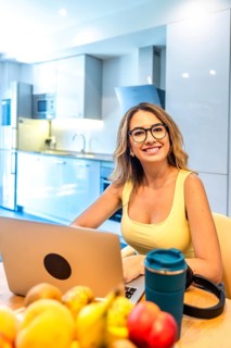 Young woman working on laptop in modern kitchen with fresh fruits, promoting healthy work life