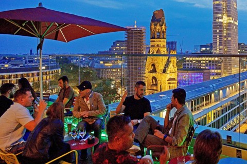 People on an outdoor terrace in the evening with a view of the illuminated Kaiser Wilhelm Memorial