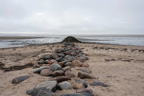 A stone groyne made of large granite blocks stretches from the sandy beach on the island of Föhr