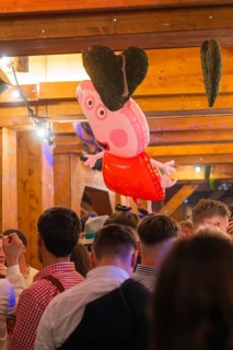 A pink heart-shaped balloon floats above a crowd in a traditional wooden house, Cannstatter Wasen