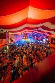 Lively celebration in a decorated beer tent with red and white stripes and lots of people,