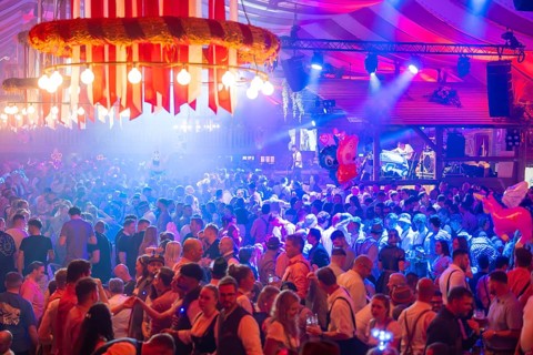 A lively party in a festive beer tent with stage and illuminated atmosphere at night, Volksfest