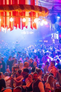Large crowd celebrating in a beer tent under colourful lights and enjoying the music, Volksfest