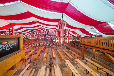 Marquee with red ceilings and wooden benches, bar in the foreground, inviting atmosphere,