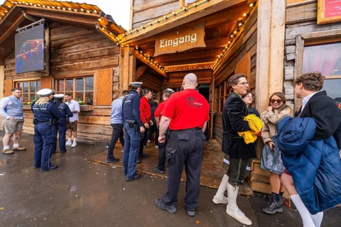 People in traditional Bavarian dress and police gather in front of a festively illuminated wooden