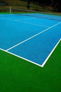 A vibrant tennis court with a blue surface contrasts against the green edges. The bright white