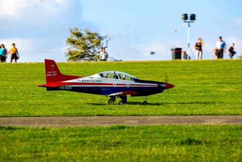 An RC model of a Pilatus PC-21 with advertising for the Swiss watch brand Breitling during a flight