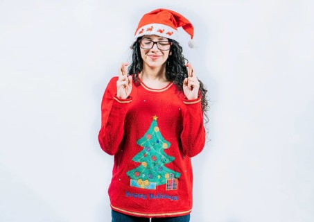 Beautiful girl in Christmas sweater making a wish isolated. Young woman in Christmas sweater making