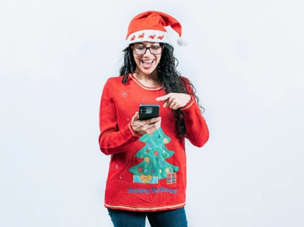 Happy girl in Christmas sweater looking pointing phone screen, isolated