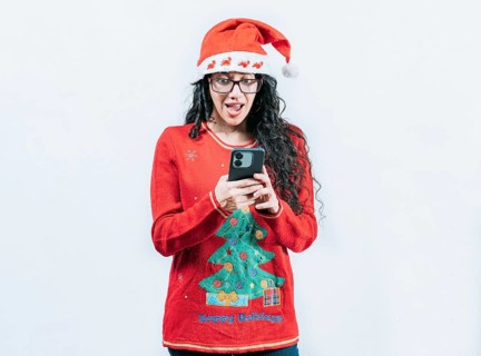 Amazed girl in Christmas hat looking at phone isolated. Surprised girl in Christmas sweater looking