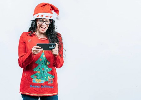 Surprised girl in Christmas sweater looking at cell phone screen, isolated. Surprised girl in