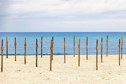 Sandy beach by the Mediterranean Sea with wooden poles for parasols and a seascape view to the