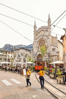 Waiters walking on a square with outdoor restaurants and an old vintage tram driving across the