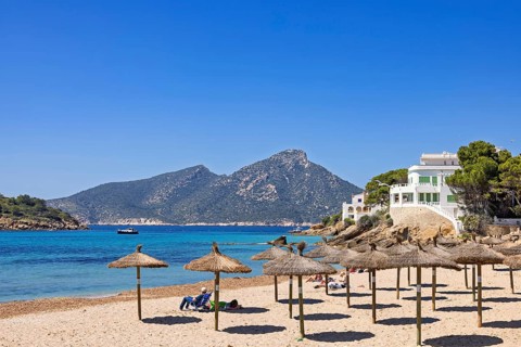 Sandy beach on the Mediterranean Sea with sun umbrellas and houses along the coast on a sunny