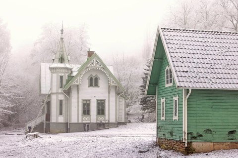 Old idyllic white wooden house with carpentry and a green garden shed on a cold winter day with