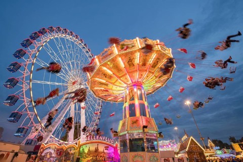 An illuminated chain carousel and Ferris wheel at night at a funfair, people swinging on chains,