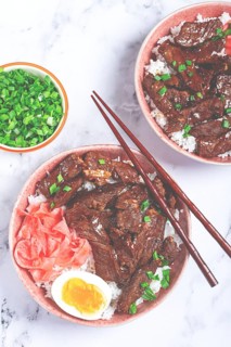 Gyudon Japanese beef with rice, pickled ginger, boiled egg slice, garnished with green onions, in a