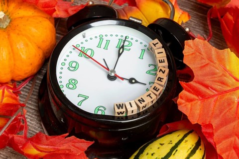 Winter time changeover: close-up of an alarm clock, autumnal decoration and letter cubes displaying