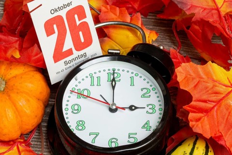 Time changeover to winter time 2025: Close-up of an alarm clock, autumnal decoration and a page