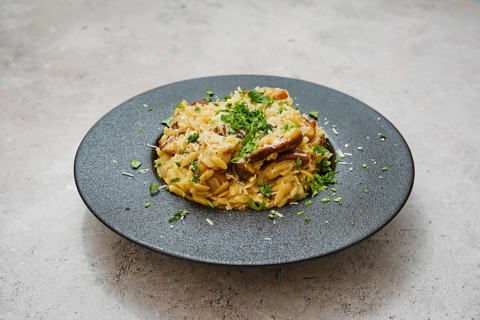 A delicious dish of risoni with porcini mushrooms is served in a sleek black bowl. Fresh herbs and