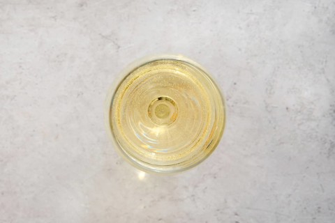 Close-up overhead view of a glass filled with white wine on a light textured surface