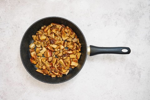 Diced porcini mushrooms are frying in a black pan, creating a savory meal. The cooking process
