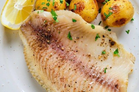 Flaky fish fillet is seasoned and served with roasted golden potatoes and fresh lemon slices. A