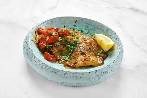 Juicy roasted red seabream fillet with tomatoes and herbs on a modern plate