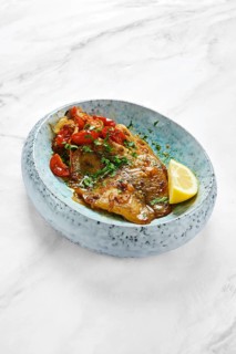 Grilled red seabream fish is topped with fresh cherry tomatoes and herbs, served with a slice of