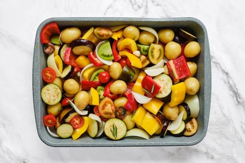 A vibrant mix of fresh vegetables is arranged in a baking tray, showcasing colorful peppers,