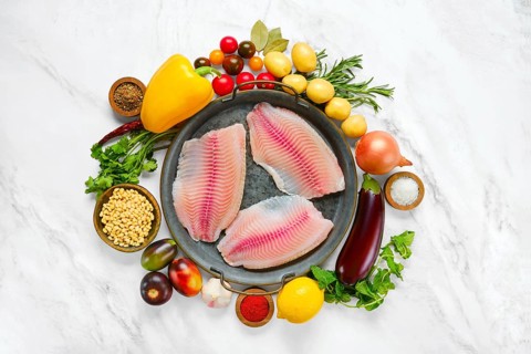 Three raw red seabream fish fillets on a round platter, surrounded by fresh vegetables like