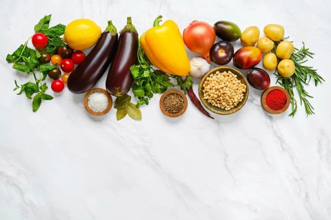 A colorful spread of fresh vegetables and herbs includes tomatoes, eggplants, cucumbers, bell