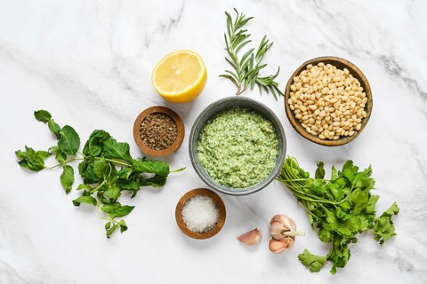 Various fresh herbs and ingredients are neatly organized on a marble surface, ready for sauce