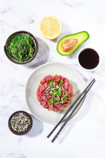 Fresh tuna tartare with avocado served on a marble table with soy sauce and seaweed salad