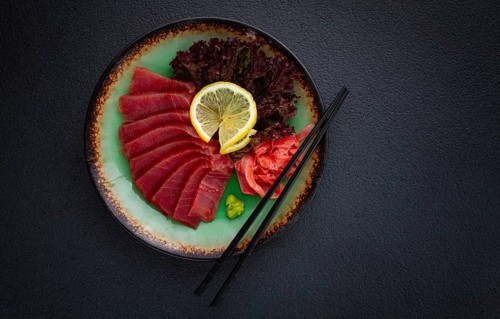 Fresh tuna sashimi served with lemon, wasabi, and pickled ginger on a dark background