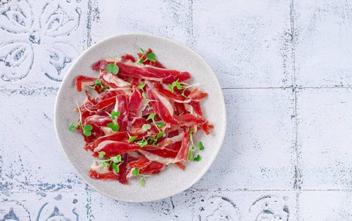 Ham of duck breast, dried duck fillet, with microgreens, plate, on a tiled table