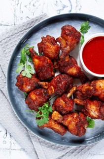 Crispy pieces of fried chicken, on a plate with sauce and herbs, in a modern kitchen environment,